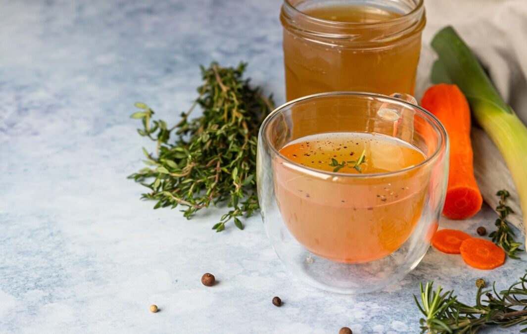 Two glass jars of brown bone broth. Herbs sitting next to them.